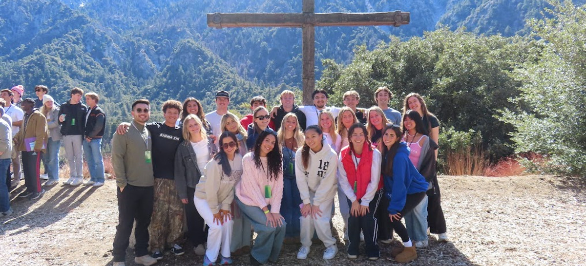 Students gathered at a mountain retreat beside a wooden cross